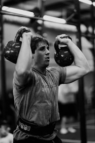 a man holding two kettles in a gym