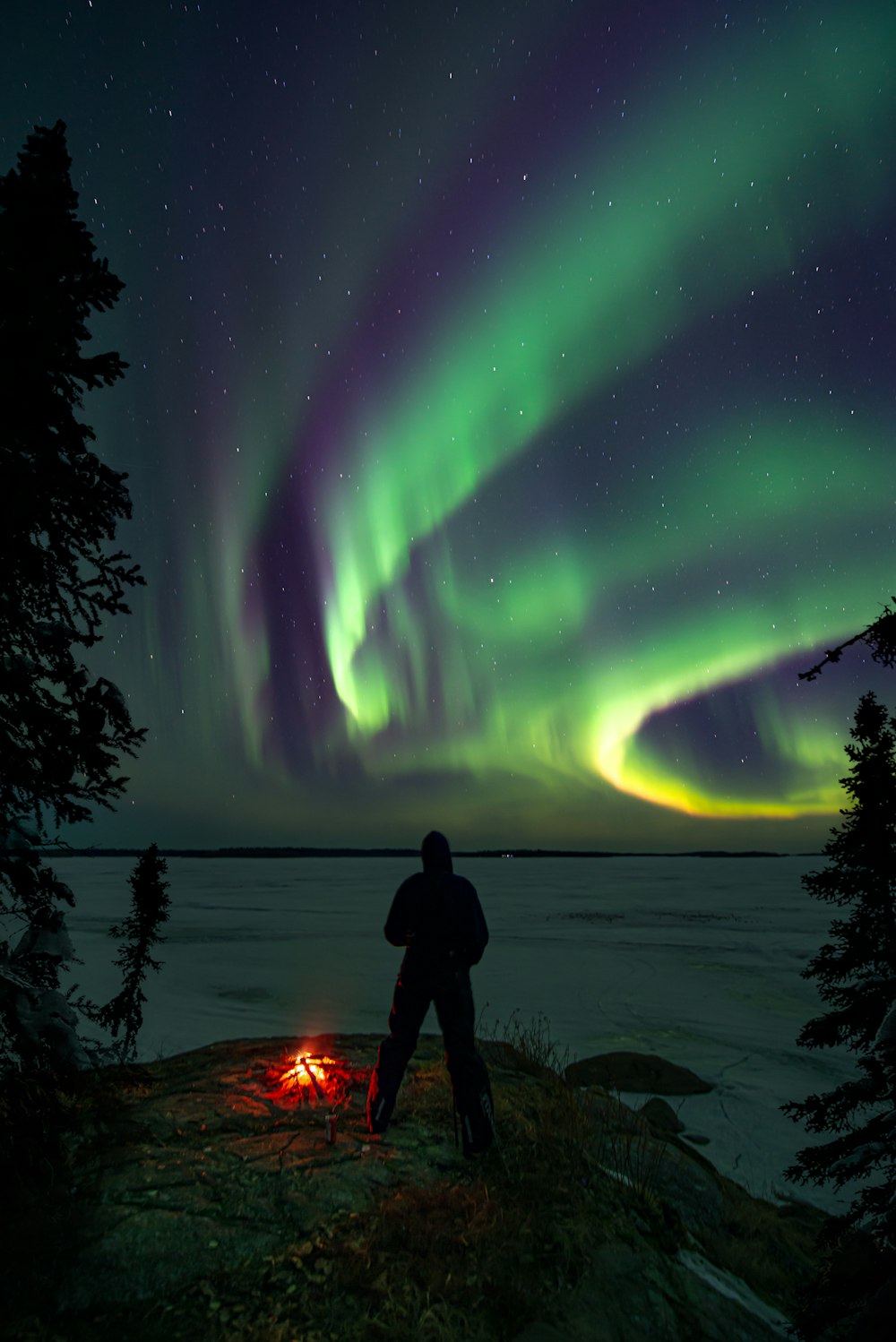 Ein Mann steht neben einem Lagerfeuer unter einer Aurora-Bohrung