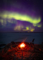 A cozy campfire scene with people enjoying a winter night under glowing northern lights