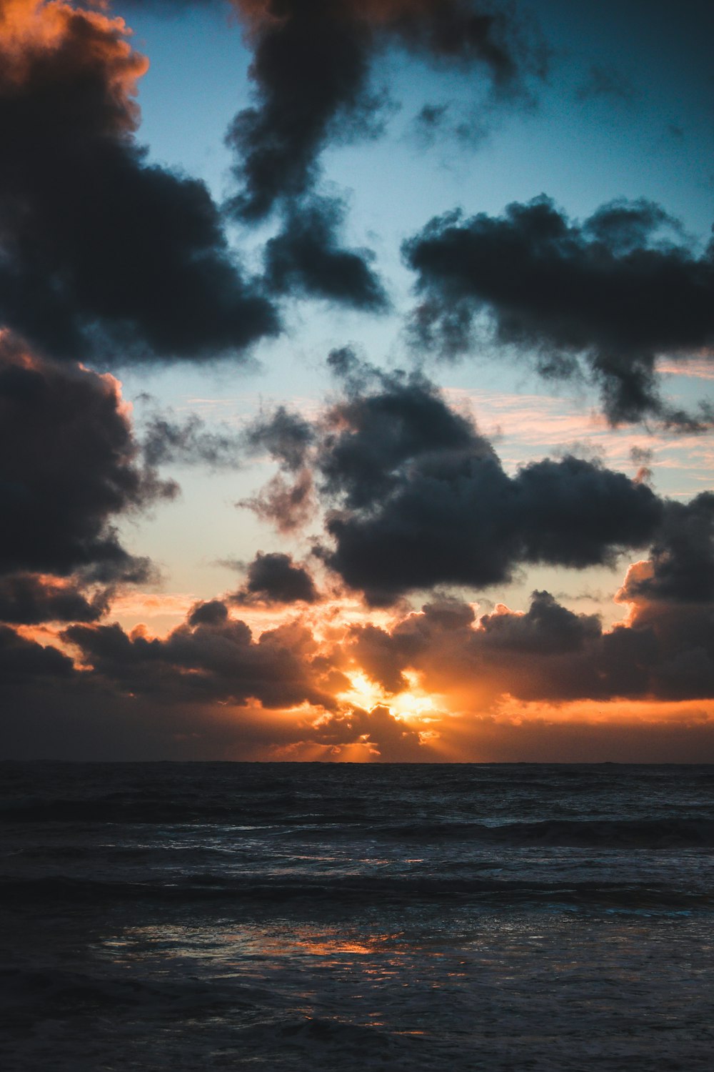 the sun is setting over the ocean on a cloudy day