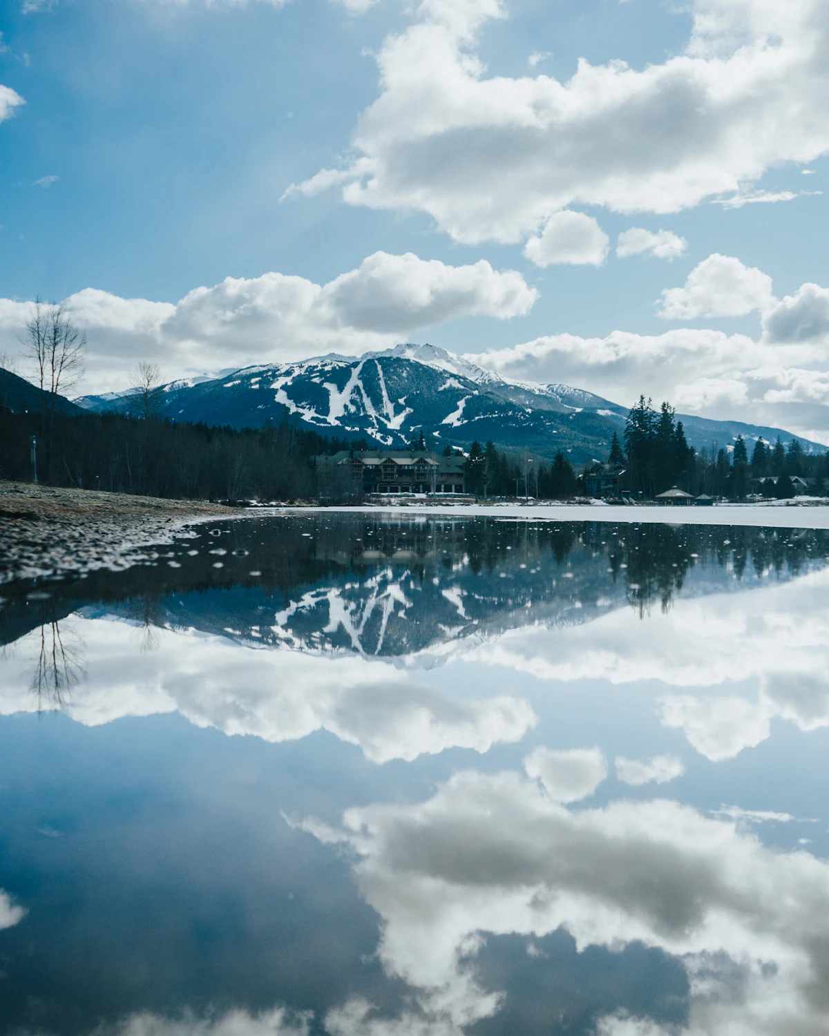 A snowy mountain and white clouds mirrored in still water in Whistler