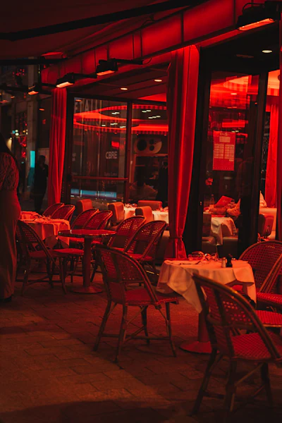 A classic Parisian restaurant interior with warm red lighting, tables and chairs