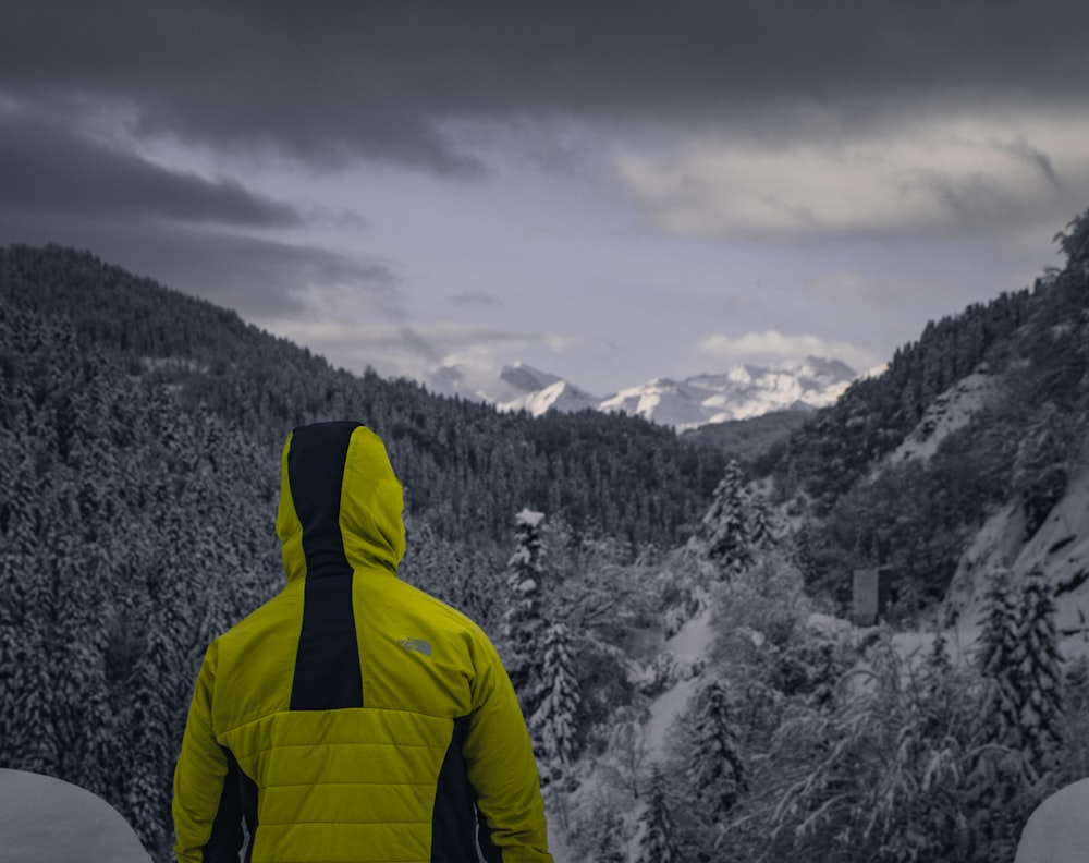 Un hombre con una chaqueta amarilla mirando una montaña nevada