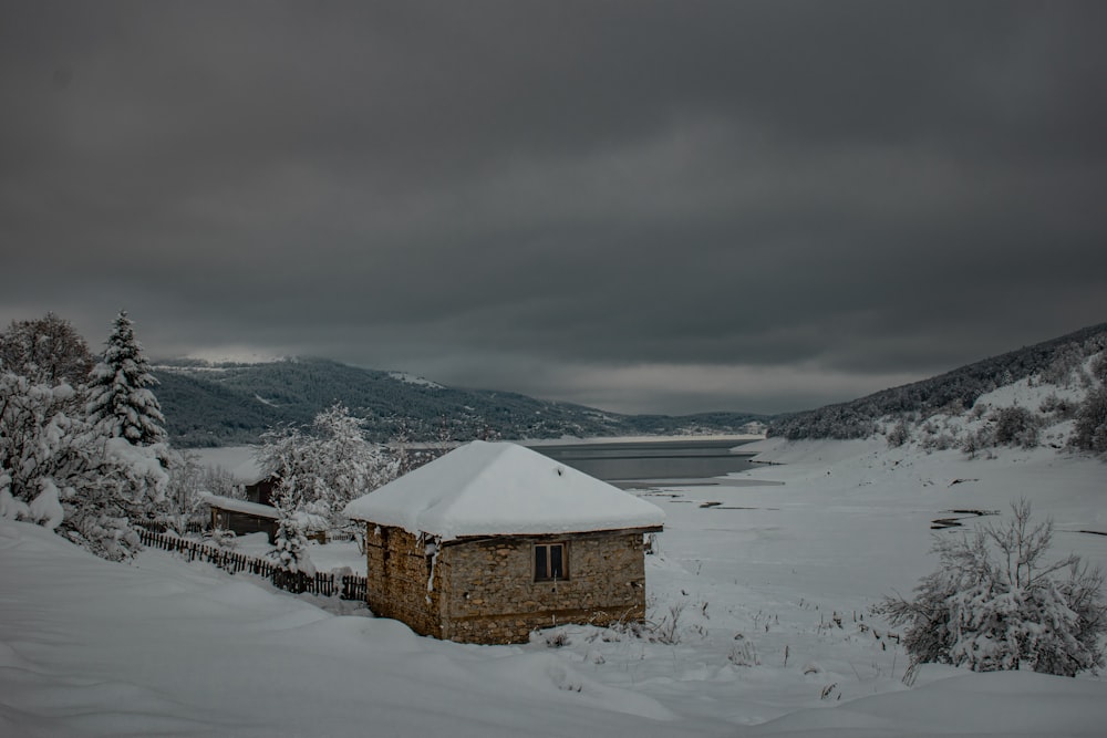 a small house covered in snow next to a body of water