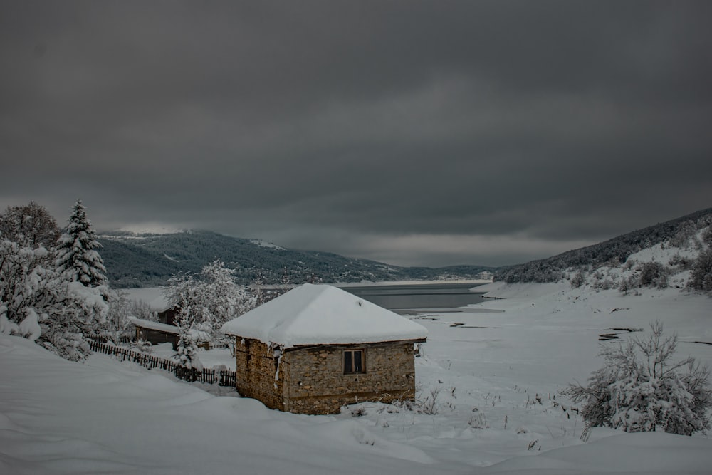 una pequeña casa cubierta de nieve junto a un cuerpo de agua