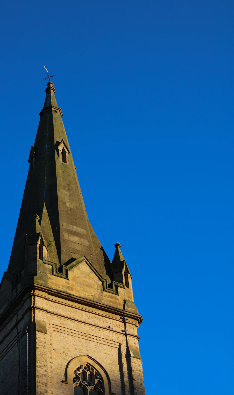 Tall stone church with pointed steeple reaching towards clear blue sky from below perspective