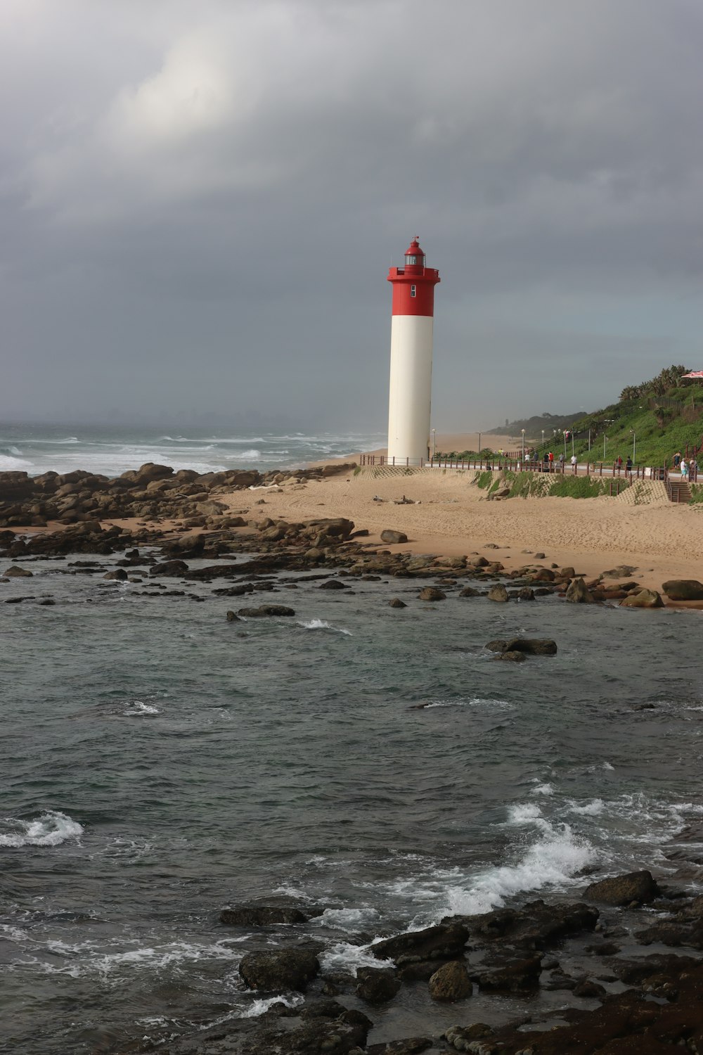 um farol vermelho e branco sentado no topo de uma praia de areia