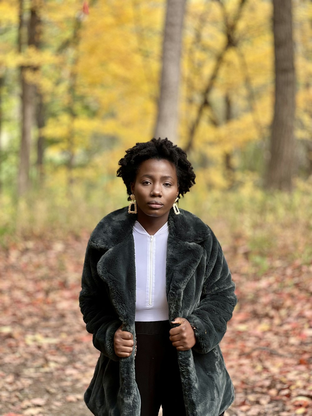 a woman standing in the woods wearing a fur coat
