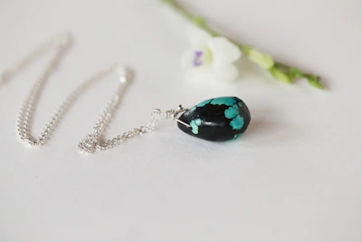 A minimalist silver necklace with a small pendant displayed on a marble surface beside a fresh flower.