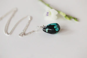 Elegant silver necklace with a turquoise pendant glowing softly against a dark background.