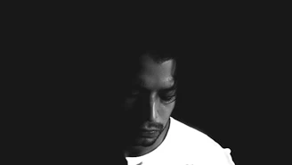 A stark, minimalist portrait of morindeezzz surrounded by shadows, with an off-white backdrop emphasizing the raw emotion in the eyes.