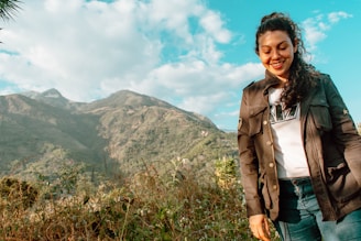 A young Brazilian woman with indigenous features smiling, standing in front of a desert landscape with a mountain of clothes in the background.