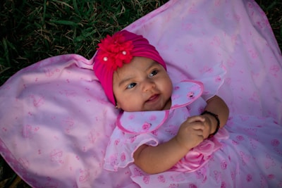 A baby girl in a soft yellow romper playing with a plush toy, wearing a delicate floral headband.