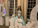 A quinceañera in a flowing dress surrounded by colorful floral decorations.