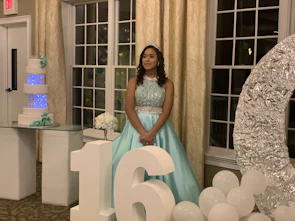 A quinceañera in a flowing dress surrounded by colorful floral decorations.