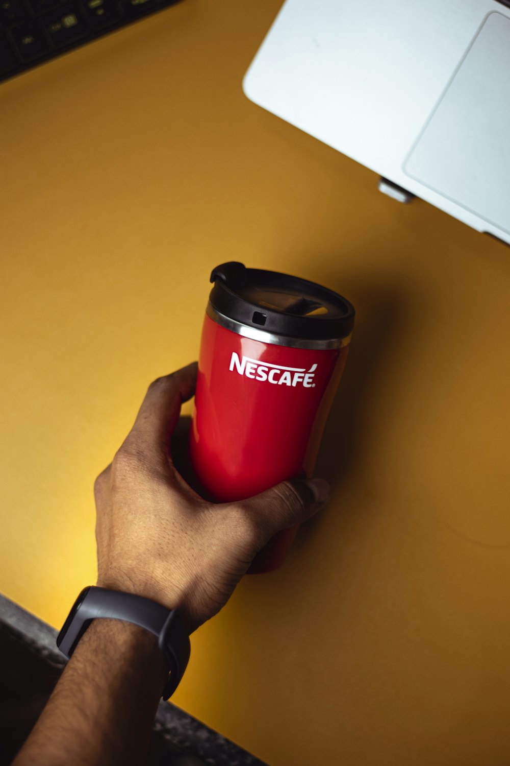a person holding a red coffee cup on top of a desk
