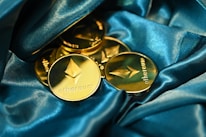 Several gold Ethereum coins are elegantly arranged on a luxurious blue satin fabric. The coins feature the Ethereum logo and the word 'ethereum' prominently engraved, giving a sense of wealth and innovation.