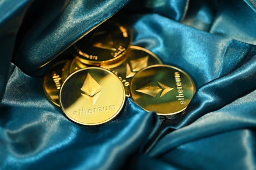 Several gold Ethereum coins are elegantly arranged on a luxurious blue satin fabric. The coins feature the Ethereum logo and the word 'ethereum' prominently engraved, giving a sense of wealth and innovation.