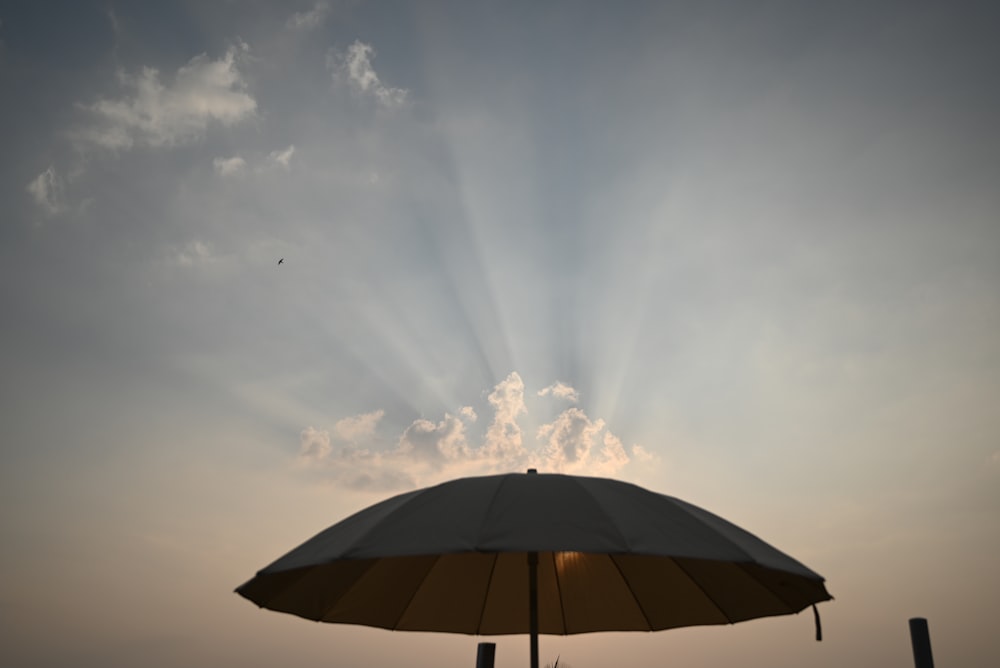 the sun is shining through the clouds over a beach umbrella