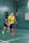 Two people playing badminton in an indoor court, with one person in a yellow shirt and the other in a black shirt. The green walls and flooring create a vibrant backdrop as they focus on their game.