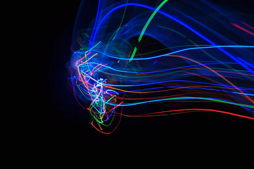 Vibrant, colorful light trails swirl against a dark background, showcasing a dynamic mixture of blue, red, and green hues. The lines form intricate patterns, creating a sense of motion and energy.
