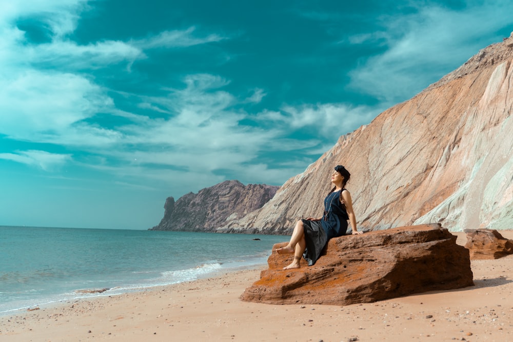 a woman sitting on a rock on the beach