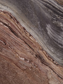 A close-up view showcases the intricate and layered patterns of sedimentary rock. The surface texture appears rough with horizontal striations and varying shades, primarily in browns and grays, suggesting a geological formation.