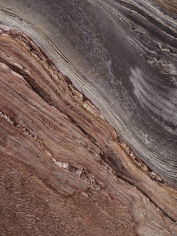 A close-up view showcases the intricate and layered patterns of sedimentary rock. The surface texture appears rough with horizontal striations and varying shades, primarily in browns and grays, suggesting a geological formation.
