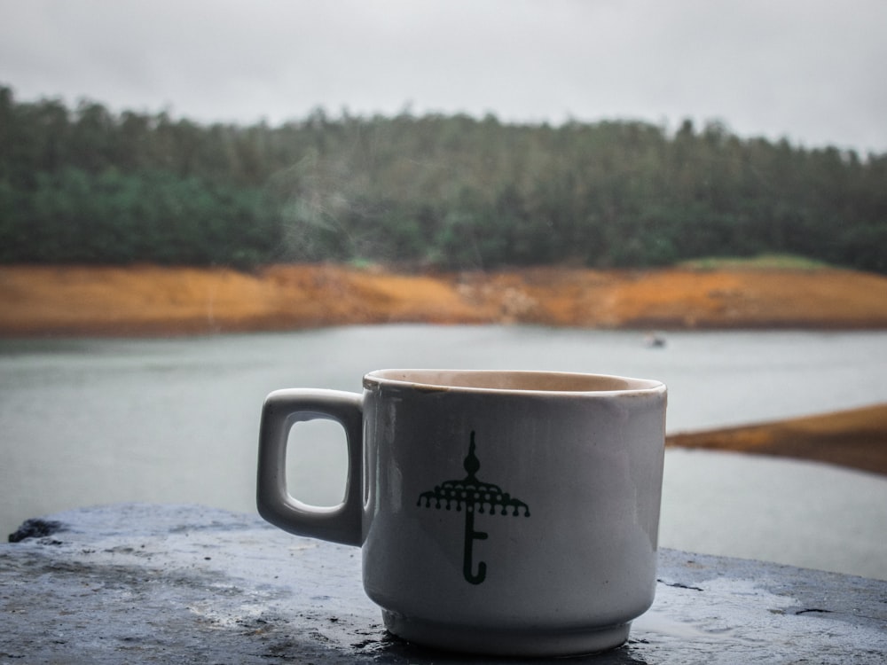 a coffee cup sitting on top of a table next to a lake