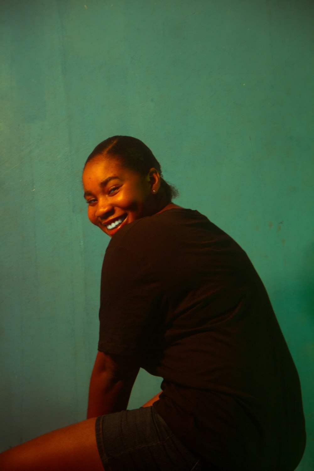 a smiling man sitting on the floor in front of a green wall