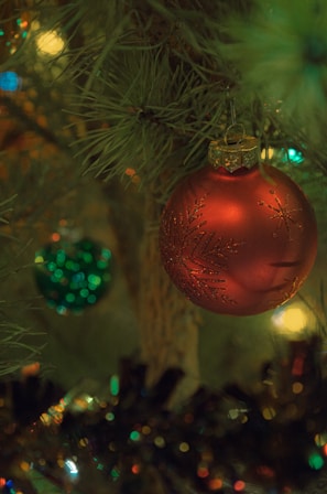 Close-up of a vibrant red and green recycled paper ornament hanging on a Christmas tree.