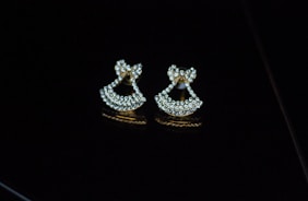Pair of refined gold earrings with small diamonds, resting on a smooth marble surface.