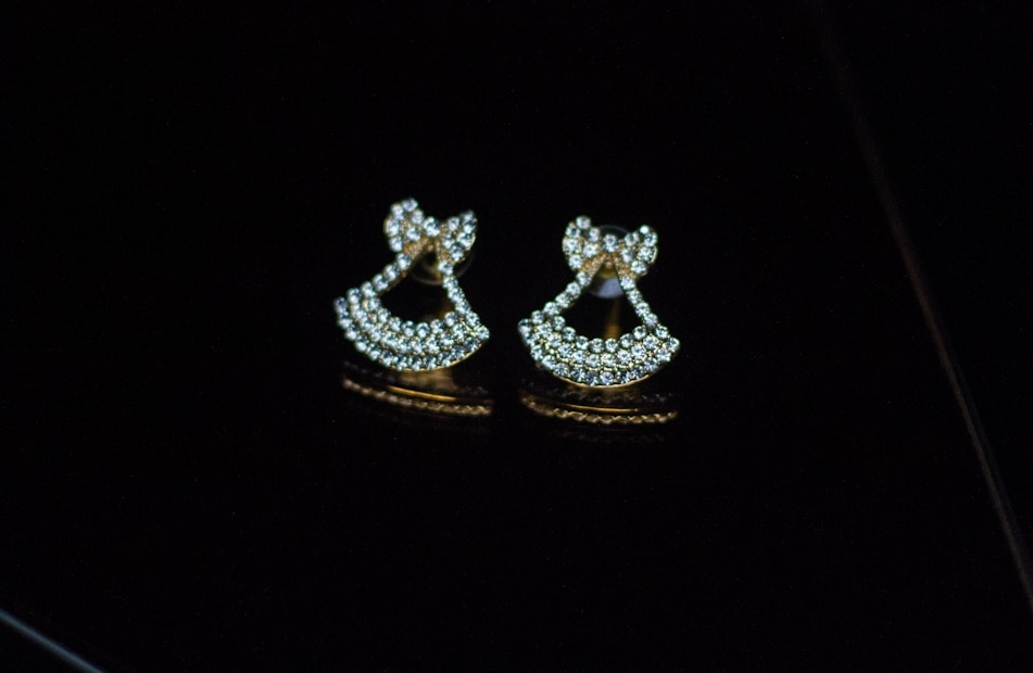 Two gold earrings adorned with sparkling diamonds are placed on a glossy black surface, creating a luxurious and elegant appearance.