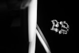 A pair of elegant earrings with pearl and rhinestone embellishments are positioned on a glossy, reflective surface, capturing intricate details and reflections. The lighting highlights the texture and shine of the jewelry against a dark background.