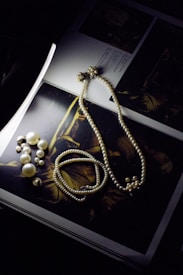 A string of pearls, a pearl bracelet, and pearl earrings are arranged on an open book featuring a dark artistic image. The lighting is low, highlighting the luster of the pearls and creating an elegant and somewhat mysterious atmosphere.