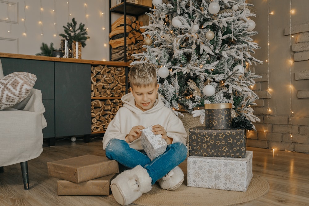a young boy sitting on the floor next to a christmas tree