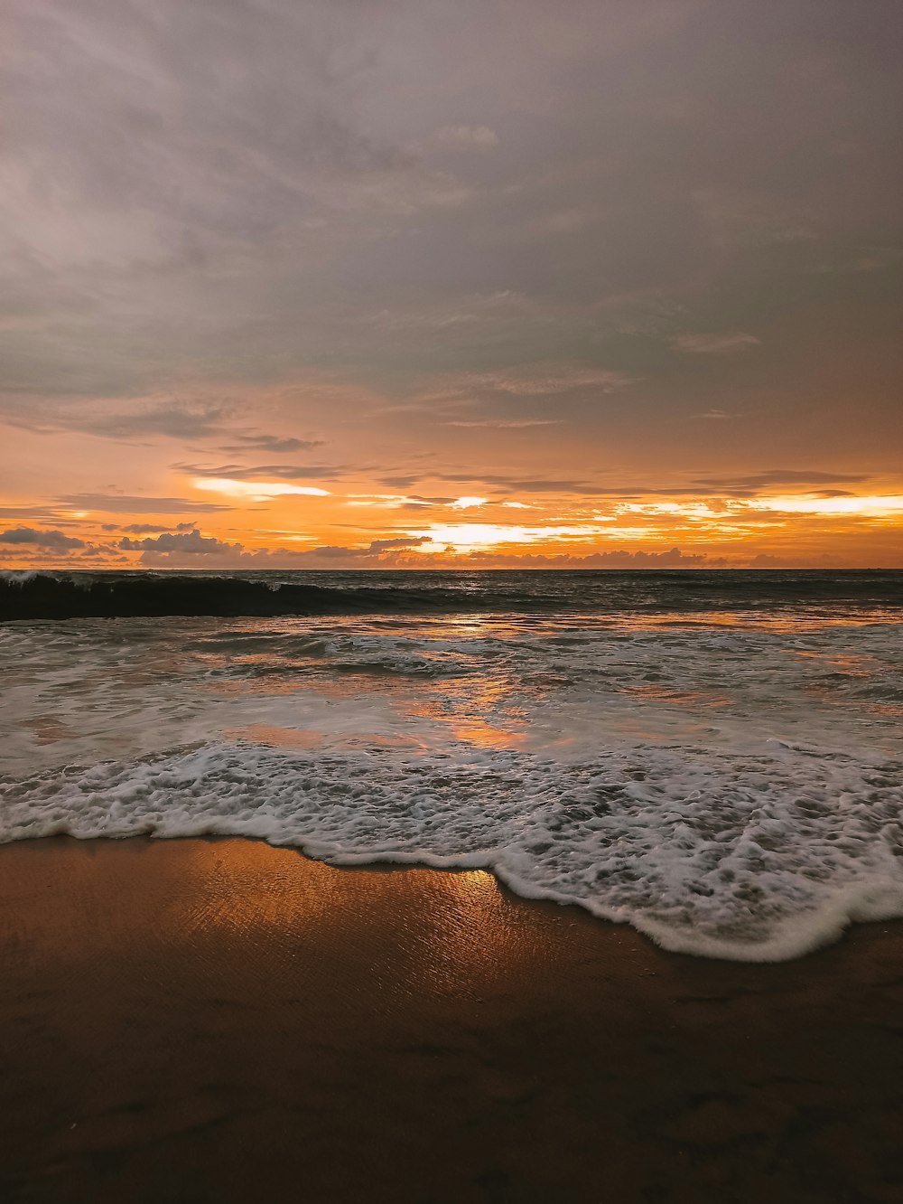 a sunset over the ocean with waves coming in