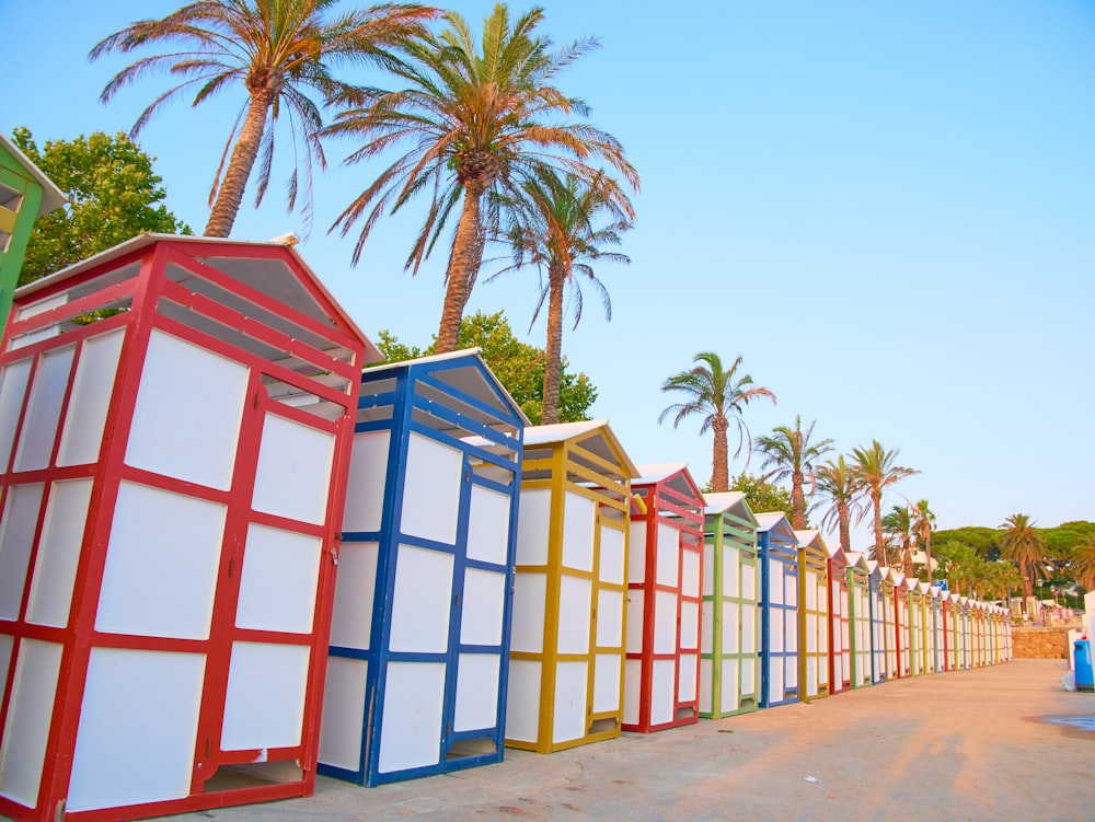 a row of brightly colored beach huts next to palm trees