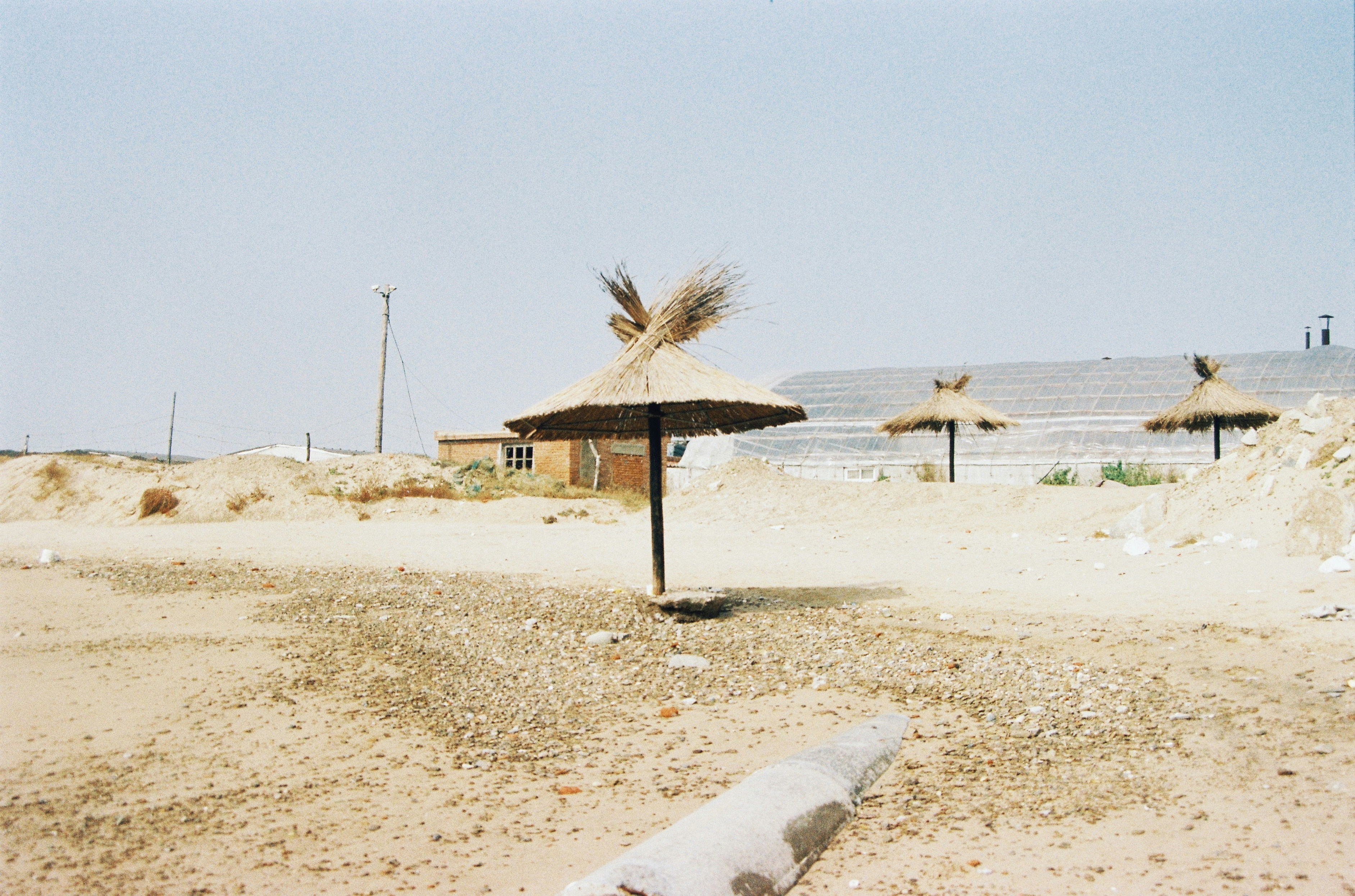 a beach with a thatched umbrella and a wooden pole