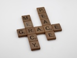 Scrabble tiles are arranged to form the words mercy, grace, and peace in a crossword pattern on a plain white background.