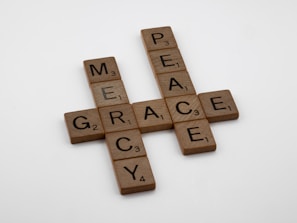 Scrabble tiles are arranged to form the words mercy, grace, and peace in a crossword pattern on a plain white background.