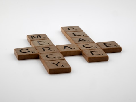 Wooden Scrabble tiles arranged on a white surface form the words 'GRACE', 'MERCY', and 'PEACE', interconnected similar to a crossword puzzle layout.