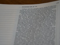 A close-up view of a page from a book, specifically from the book of Nehemiah 8:12. The text is slightly blurred towards the bottom, with clear headings and verses that discuss topics related to food, celebration, and religious events. The page includes a column of dotted lines on the left.