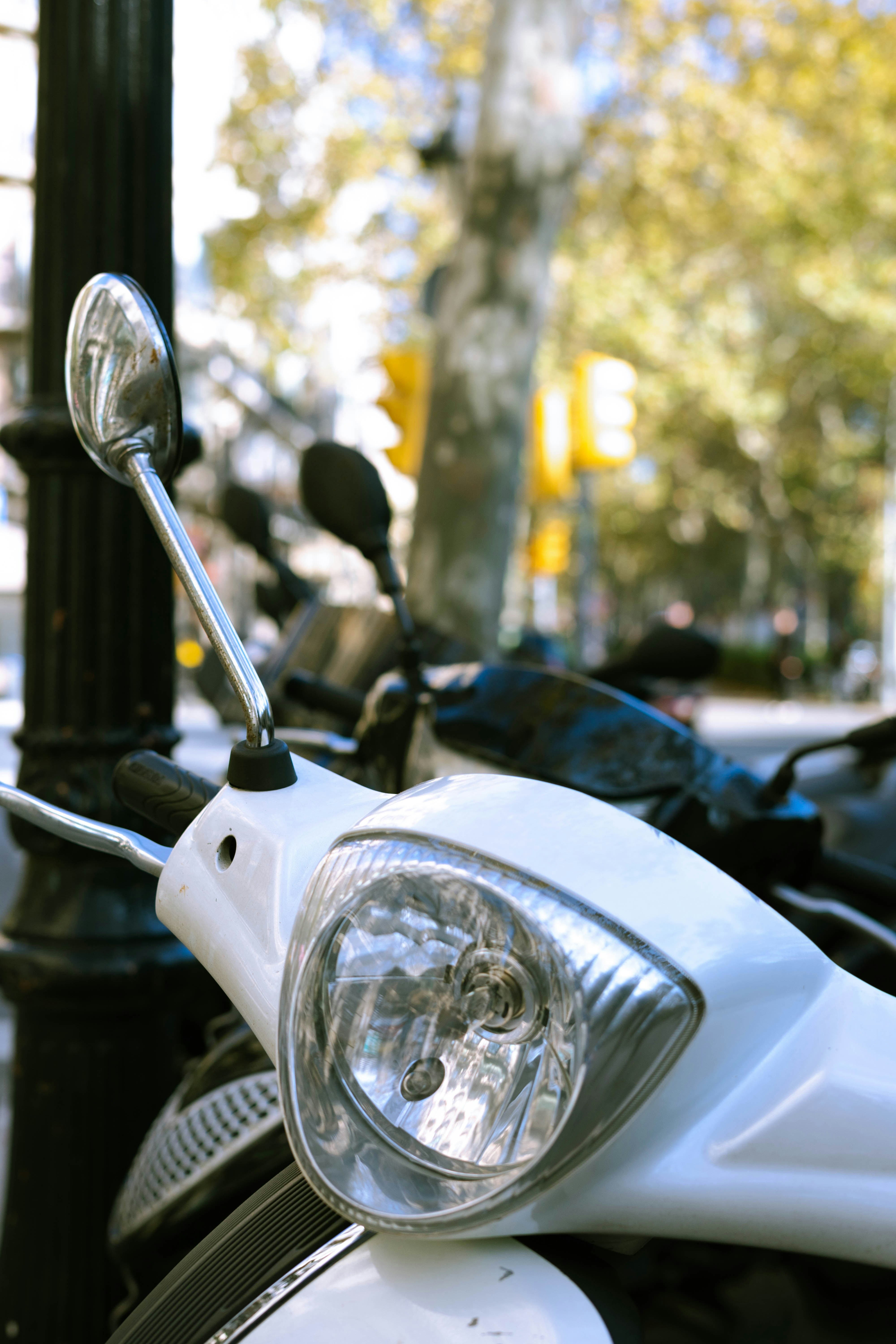 Close-up of a white moped's headlamp and mirror on a city street