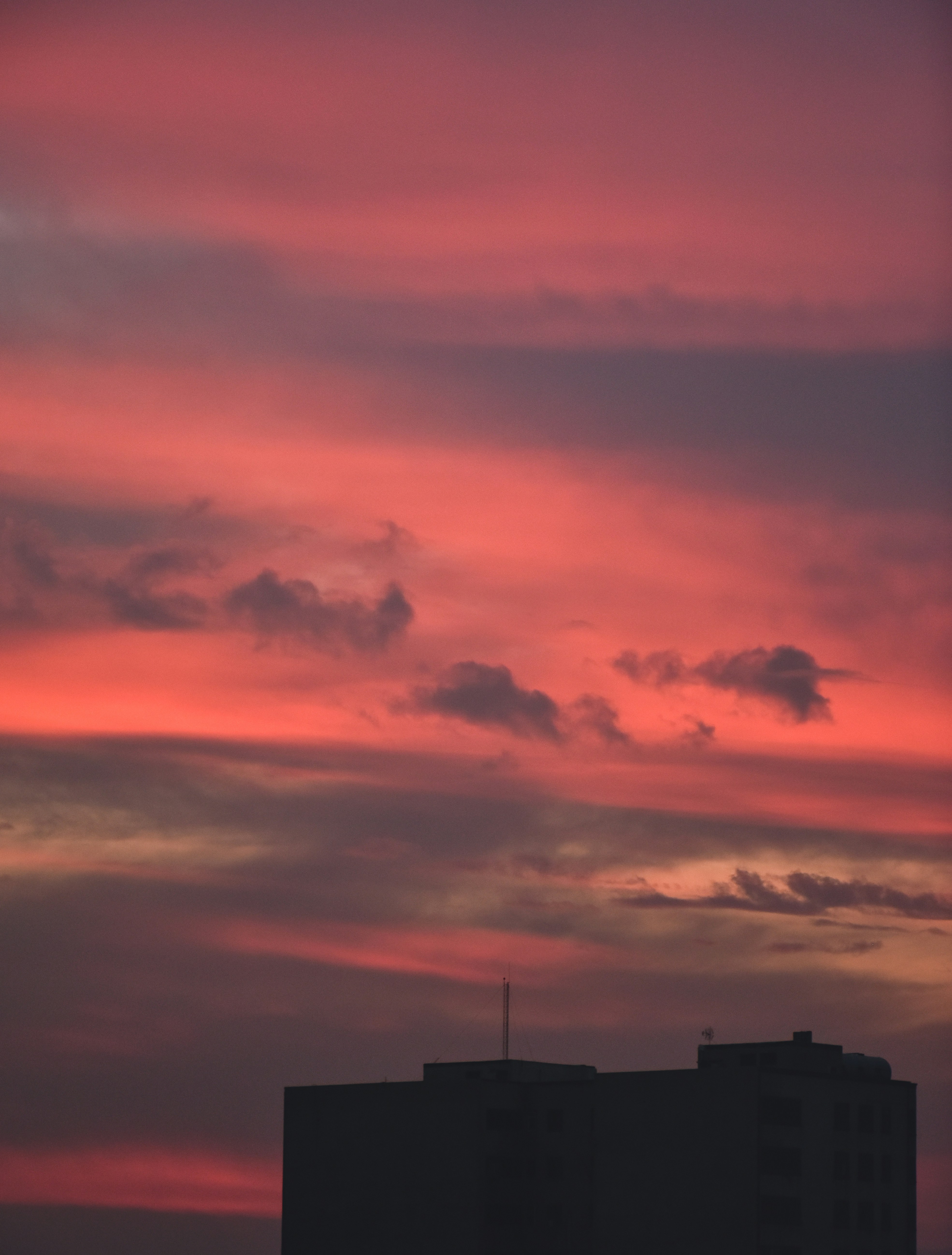a red and pink sky with a building in the foreground