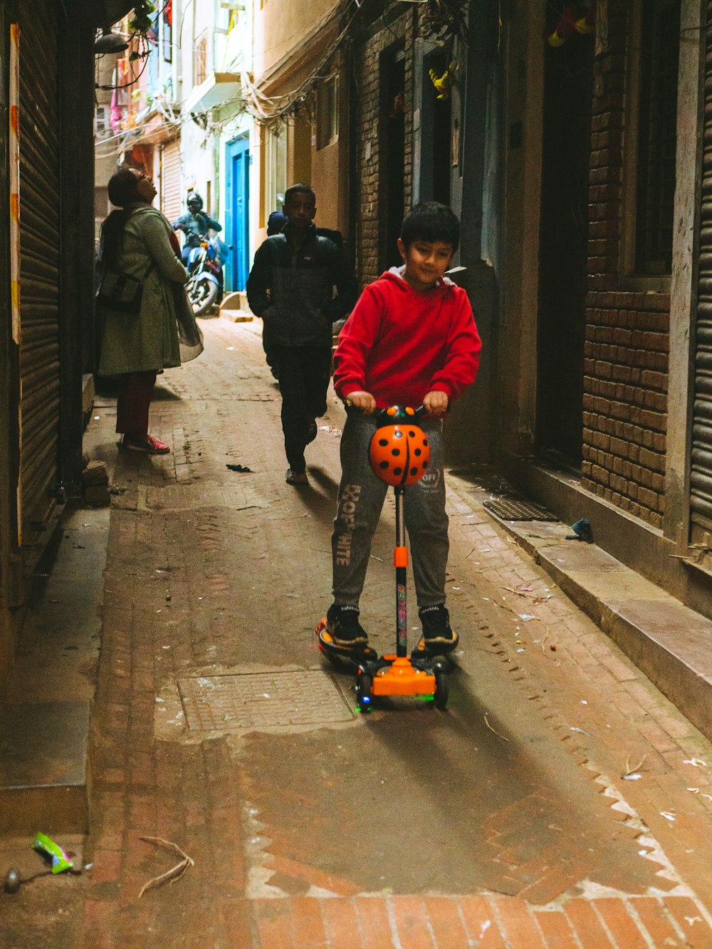 a young boy riding a scooter down a narrow street