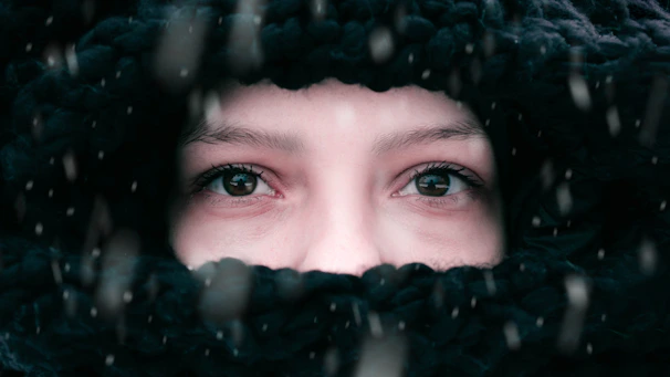 A close-up of a chunky knit scarf wrapped around a person's neck on a snowy day.