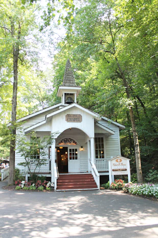 The charming white chapel nestled among tall trees, bathed in warm afternoon light.