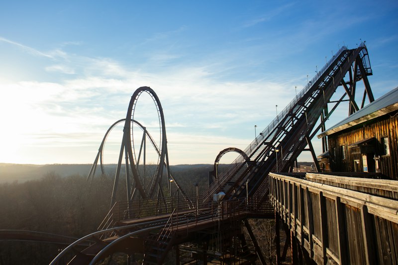 Steel roller coaster track twisting into a tall vertical loop above a wooden boardwalk, with hazy forested hills and a low sun behind