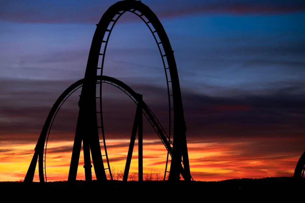 the silhouette of a roller coaster at sunset